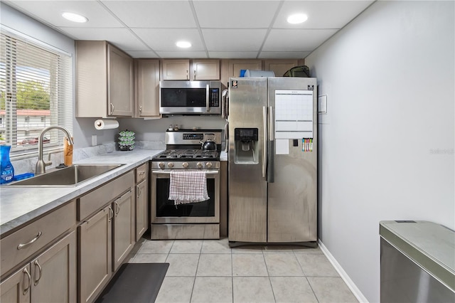 kitchen featuring baseboards, a drop ceiling, appliances with stainless steel finishes, a sink, and light tile patterned flooring