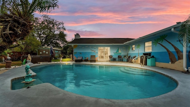 pool at dusk featuring a jacuzzi, an outdoor pool, and a patio