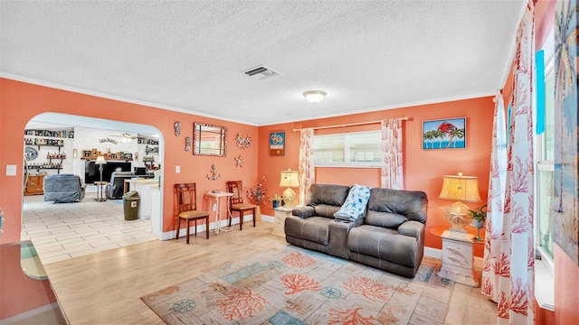 living room with visible vents, arched walkways, ornamental molding, a textured ceiling, and light wood-type flooring