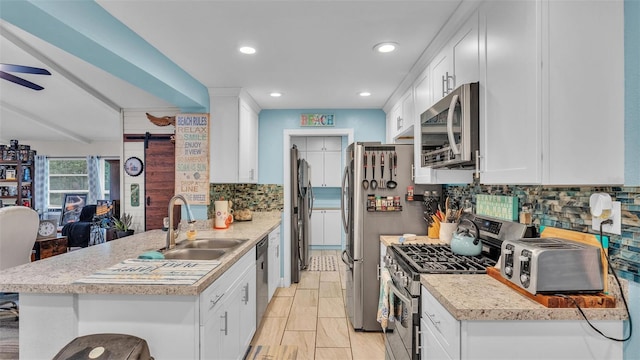 kitchen featuring a barn door, stainless steel appliances, a peninsula, a sink, and white cabinetry