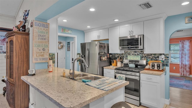 kitchen featuring a peninsula, a sink, visible vents, white cabinets, and appliances with stainless steel finishes