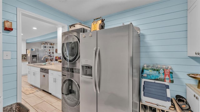 kitchen featuring light stone counters, stainless steel appliances, stacked washer / drying machine, white cabinets, and a sink