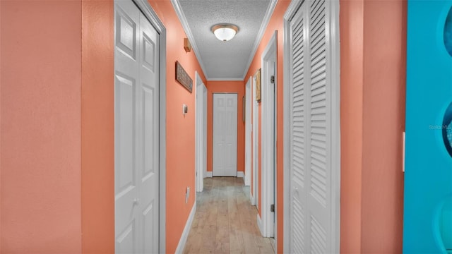 corridor with light wood-style floors, a textured ceiling, and baseboards