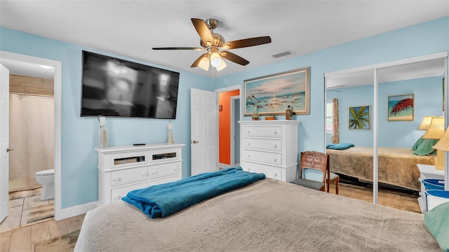 bedroom featuring visible vents, a ceiling fan, ensuite bath, wood finished floors, and a closet