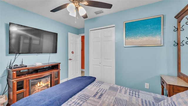 bedroom with ceiling fan, visible vents, a closet, and a glass covered fireplace