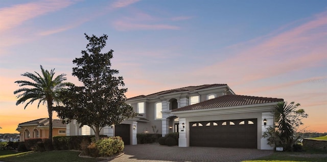 mediterranean / spanish-style home with a garage, decorative driveway, a tile roof, and stucco siding