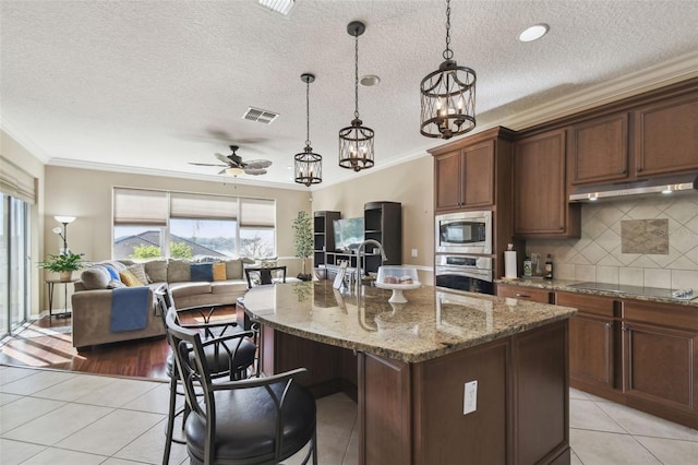 kitchen with light tile patterned floors, visible vents, open floor plan, stainless steel appliances, and under cabinet range hood