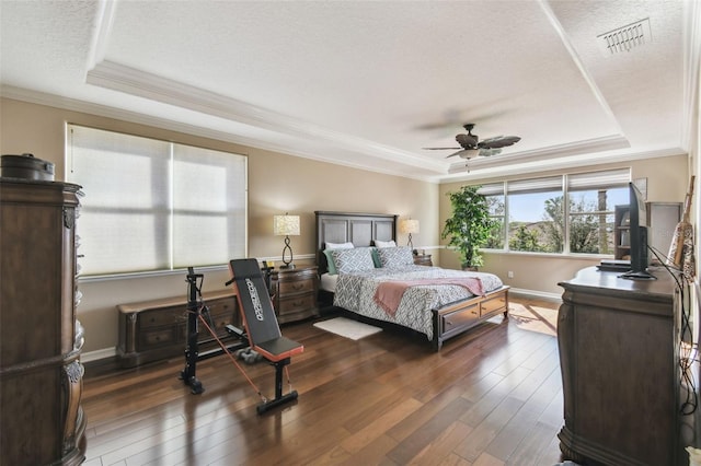 bedroom with dark wood-style floors, a tray ceiling, visible vents, and ornamental molding