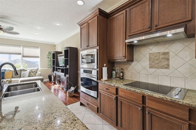 kitchen featuring under cabinet range hood, stainless steel appliances, a sink, tasteful backsplash, and crown molding