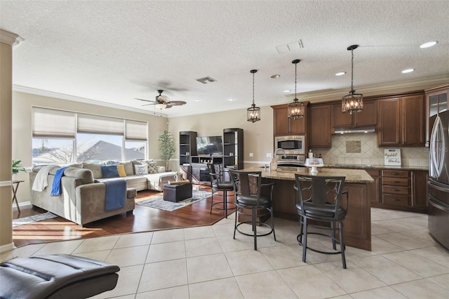 kitchen featuring light tile patterned floors, visible vents, a breakfast bar, open floor plan, and stainless steel appliances