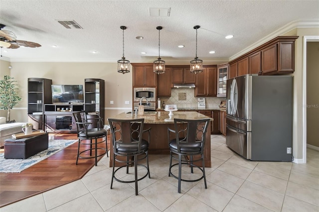 kitchen with light tile patterned floors, stainless steel appliances, visible vents, backsplash, and a center island with sink