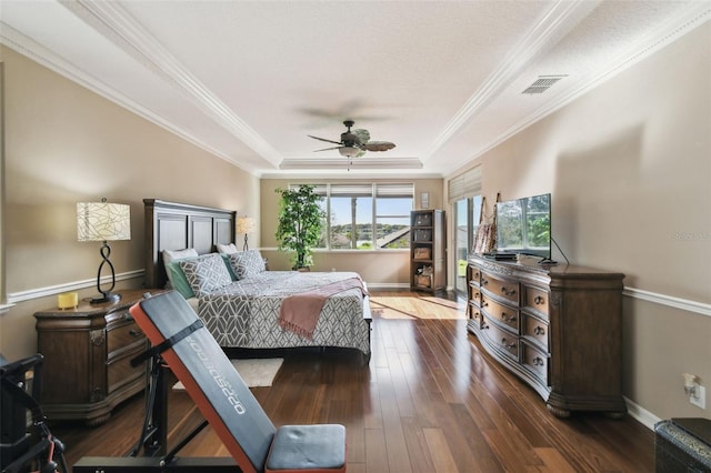 bedroom with ornamental molding, a tray ceiling, dark wood-type flooring, and baseboards