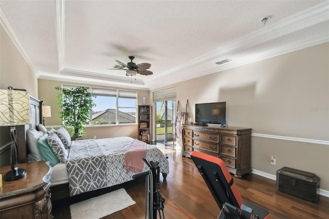 bedroom featuring wood finished floors, visible vents, baseboards, a tray ceiling, and crown molding