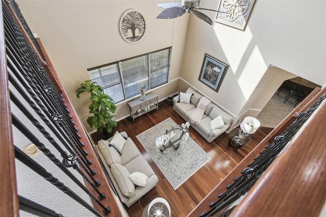 living room with a ceiling fan, a towering ceiling, baseboards, and wood finished floors