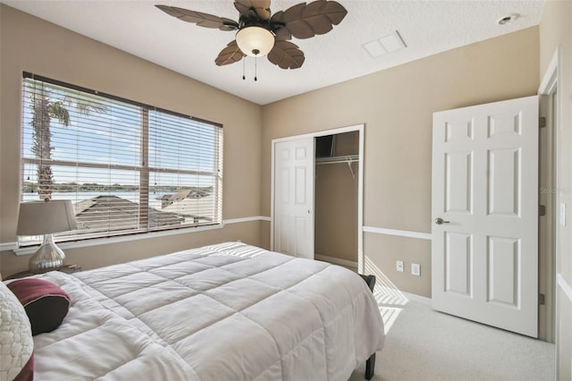 carpeted bedroom with a closet, multiple windows, ceiling fan, and a textured ceiling