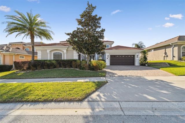 mediterranean / spanish house with a garage, a tiled roof, decorative driveway, a front yard, and stucco siding