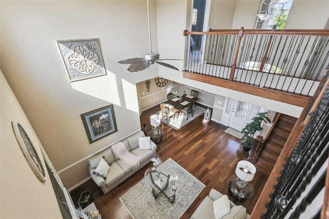 living room featuring a towering ceiling, baseboards, a ceiling fan, and wood finished floors