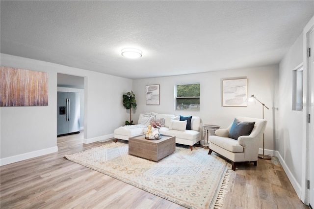 living area featuring baseboards, light wood finished floors, and a textured ceiling