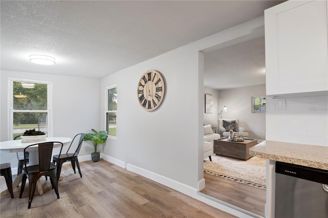 dining space featuring baseboards, a textured ceiling, and light wood finished floors