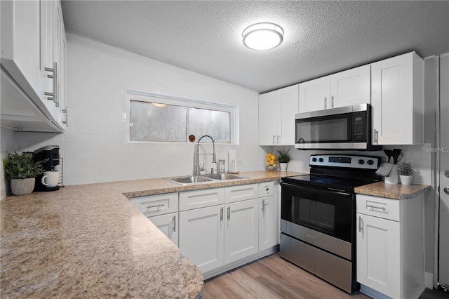 kitchen with light wood finished floors, electric range, a sink, white cabinets, and stainless steel microwave