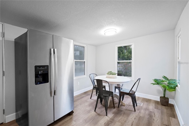 dining room with a textured ceiling, light wood-type flooring, and baseboards