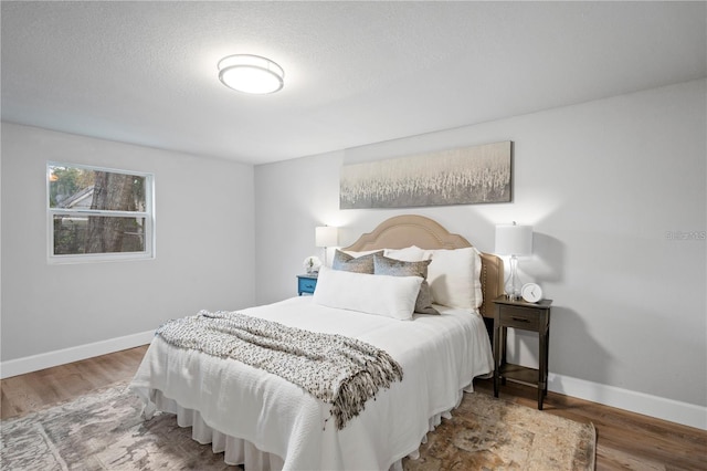 bedroom featuring wood finished floors, baseboards, and a textured ceiling