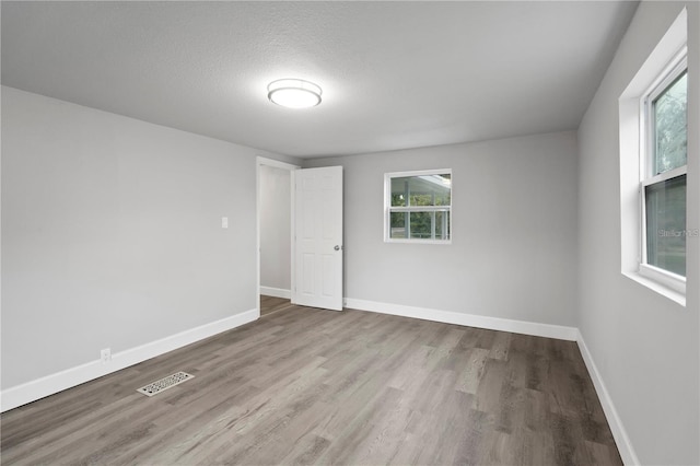 empty room featuring visible vents, baseboards, a textured ceiling, and wood finished floors