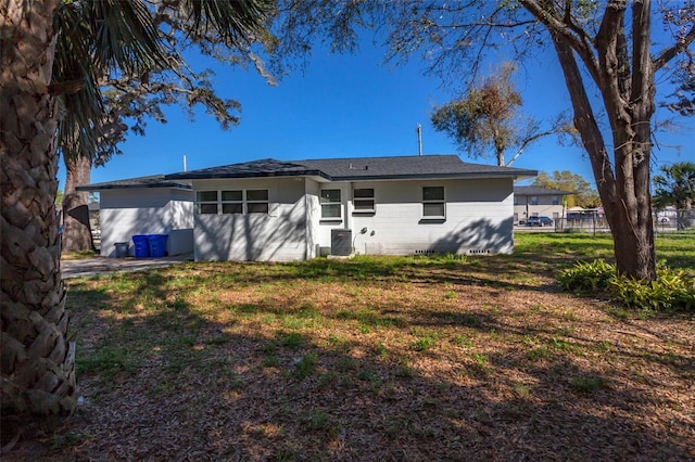 rear view of property with central AC, fence, and a lawn