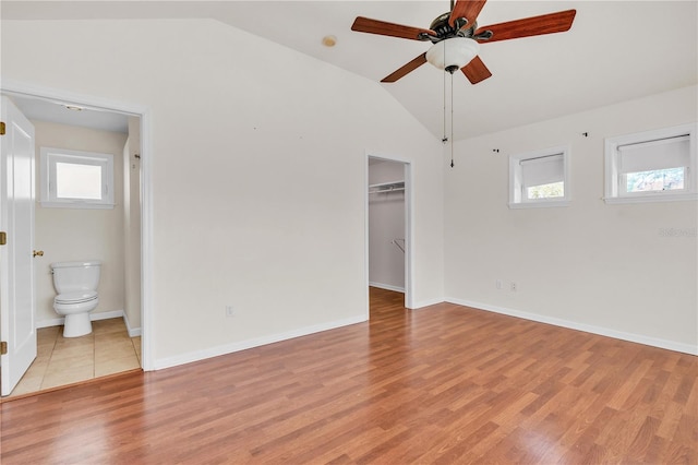 unfurnished bedroom featuring vaulted ceiling, a spacious closet, light wood-style flooring, and baseboards