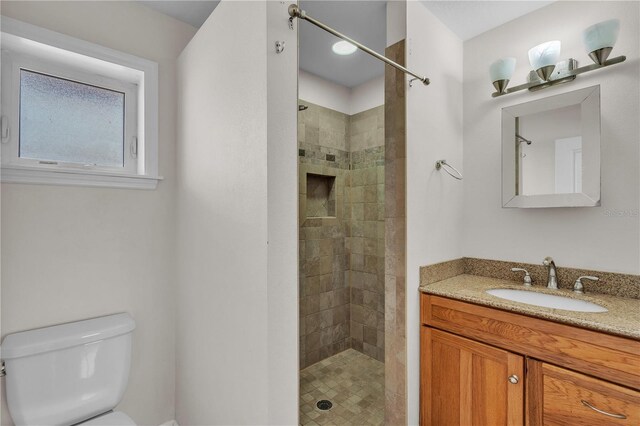 bathroom featuring toilet, tiled shower, and vanity