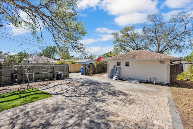 rear view of property with a patio, roof with shingles, and fence