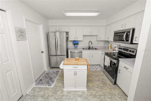 kitchen with stainless steel appliances, white cabinets, a sink, a kitchen island, and butcher block countertops