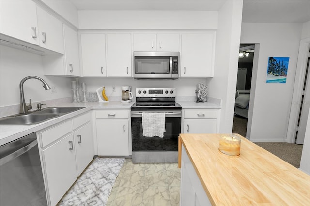 kitchen with appliances with stainless steel finishes, butcher block countertops, a sink, and white cabinetry