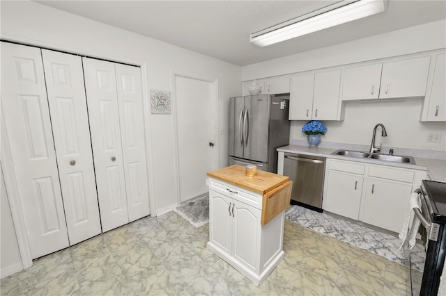 kitchen with butcher block countertops, a sink, white cabinets, marble finish floor, and appliances with stainless steel finishes