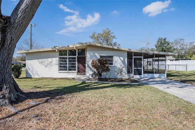 mid-century modern home featuring concrete driveway, a sunroom, an attached carport, fence, and a front lawn