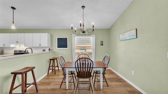 dining space with baseboards, a textured ceiling, an inviting chandelier, and light wood finished floors