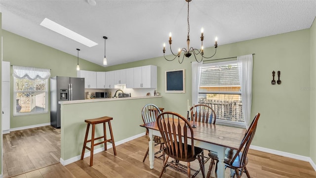 dining room with baseboards, vaulted ceiling with skylight, light wood-style floors, and a textured ceiling