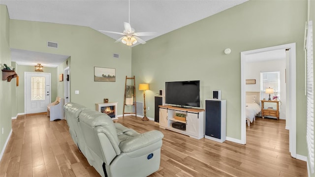 living room with a glass covered fireplace, visible vents, light wood finished floors, and ceiling fan