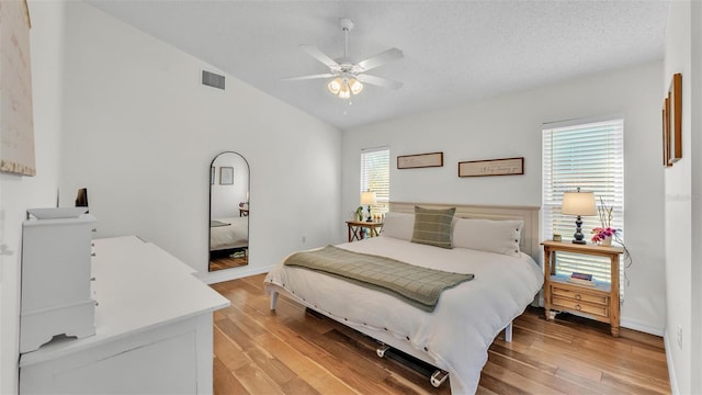 bedroom featuring visible vents, a ceiling fan, a textured ceiling, light wood-style floors, and vaulted ceiling