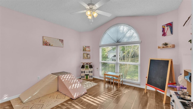 rec room with baseboards, lofted ceiling, wood finished floors, a textured ceiling, and a ceiling fan