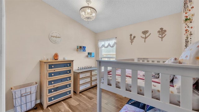 bedroom with a chandelier, a textured ceiling, wood finished floors, and vaulted ceiling