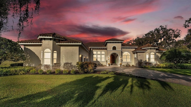 mediterranean / spanish home with a tiled roof, stucco siding, driveway, and a front yard