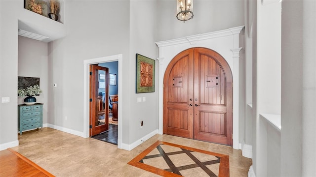 foyer entrance with arched walkways, a notable chandelier, baseboards, and a towering ceiling