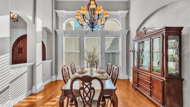 dining space featuring a notable chandelier, light wood-style flooring, a high ceiling, and baseboards