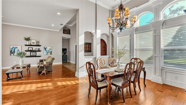 dining space featuring ornamental molding, a high ceiling, an inviting chandelier, light wood-style floors, and arched walkways