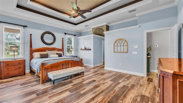 bedroom featuring a raised ceiling, multiple windows, and light wood-type flooring