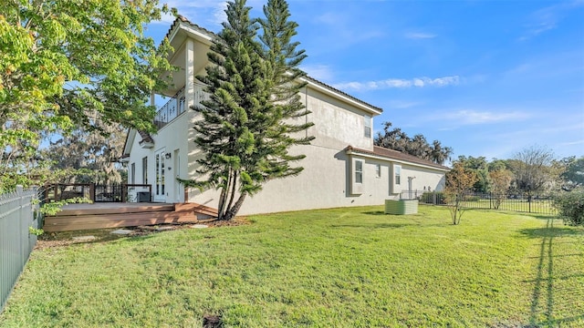 view of side of home with stucco siding, a lawn, a deck, and fence