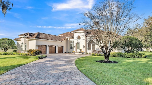 mediterranean / spanish-style home with a tiled roof, a front yard, stucco siding, decorative driveway, and a garage