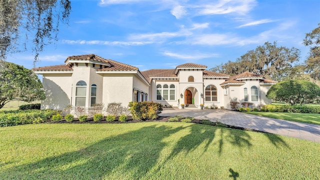 mediterranean / spanish-style house with decorative driveway, a tile roof, a front yard, and stucco siding