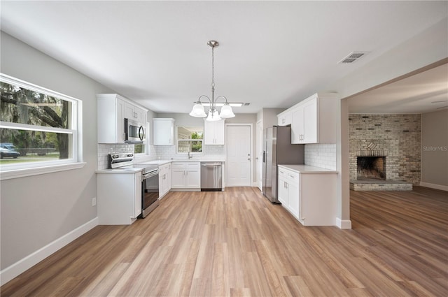 kitchen featuring visible vents, decorative backsplash, a fireplace, light wood-style floors, and stainless steel appliances